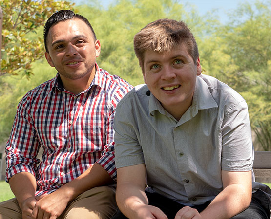 Two young men sitting together at a park and smiling at the camera