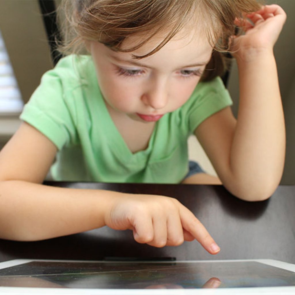 Young girl in a light green shirt pointing to something on a table