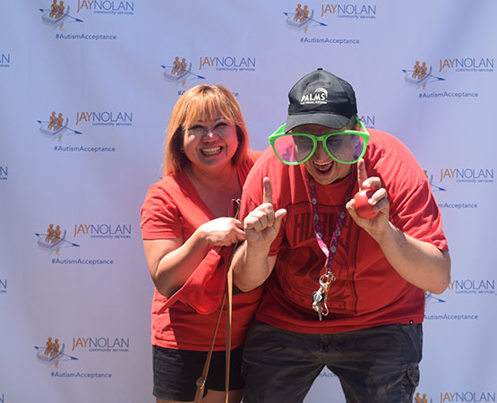 Man and woman wearing red smiling in front of a screen with JNCS logos