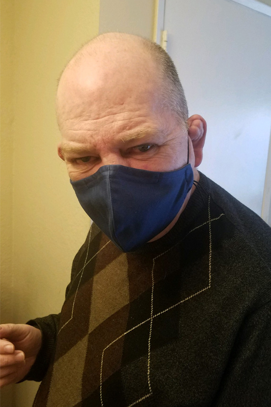 Bald man in a checkered sweater wearing a blue facemask