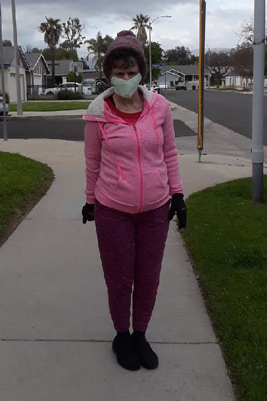 Woman in a pink jacket wearing a facemask and standing on the corner of a residential neighborhood