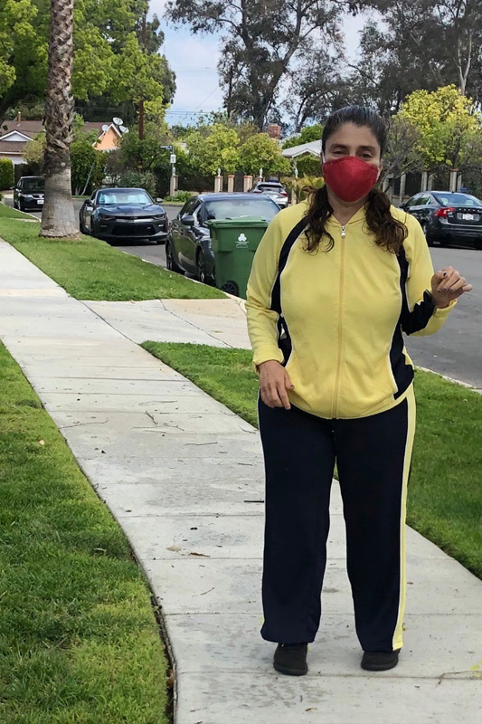Woman in a yellow jacket wearing a red facemask standing on the street