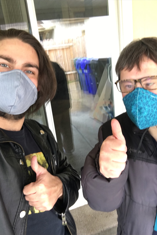 Two people wearing blue facemasks giving a thumbs up to the camera