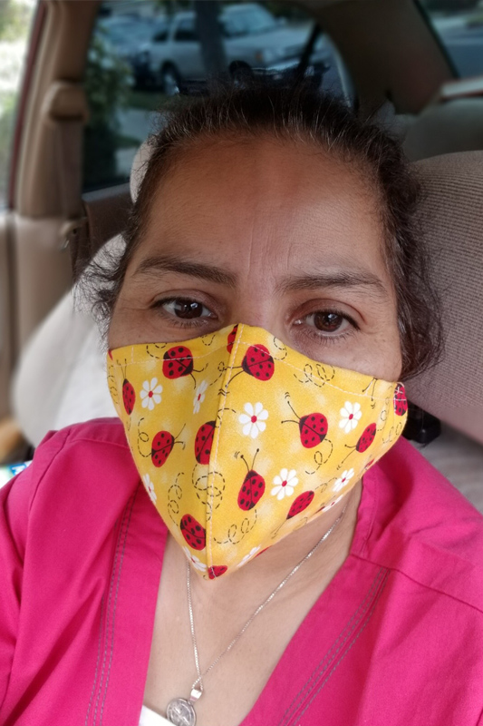 Woman in a pink shirt wearing a yellow facemask with a pattern of ladybugs and white flowers