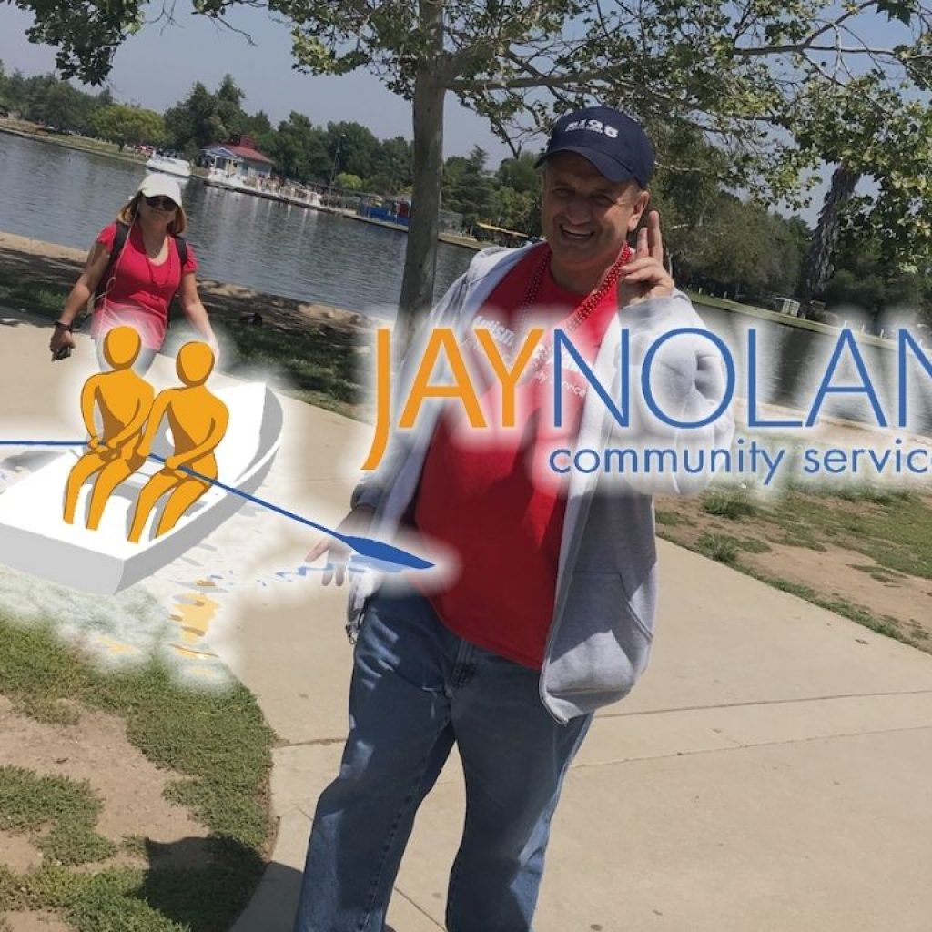 Man in red shirt walking through the park with a lake behind him with JNCS logo overlaid