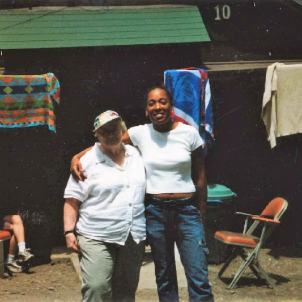 Ann and another woman smiling in front of a cabin at the JNCS camp