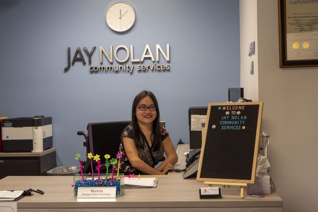 JNCS Receptionist Mariela smiling from her seat at the front desk of the JNCS main office.