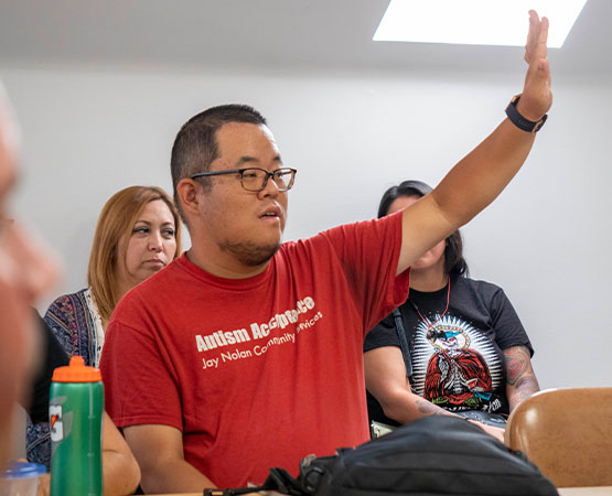 Hunter raising his hand at a meeting while wearing an Autism Acceptance shirt