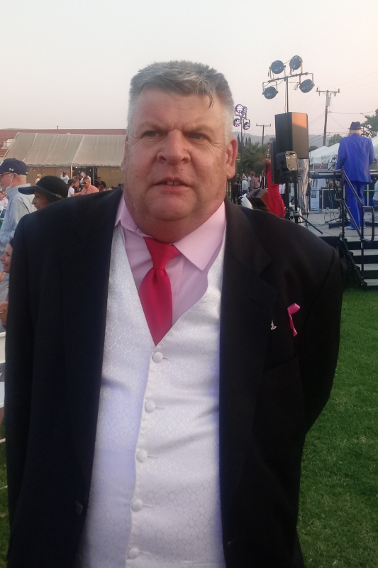 Martin in a black suit with a pink dress shirt and red tie at an outdoor event.