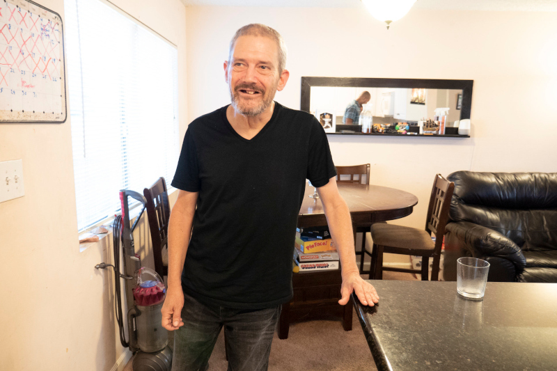 Rob Freeman, an older caucasian man with short grey hair and beard wearing a black shirt while standing in his home