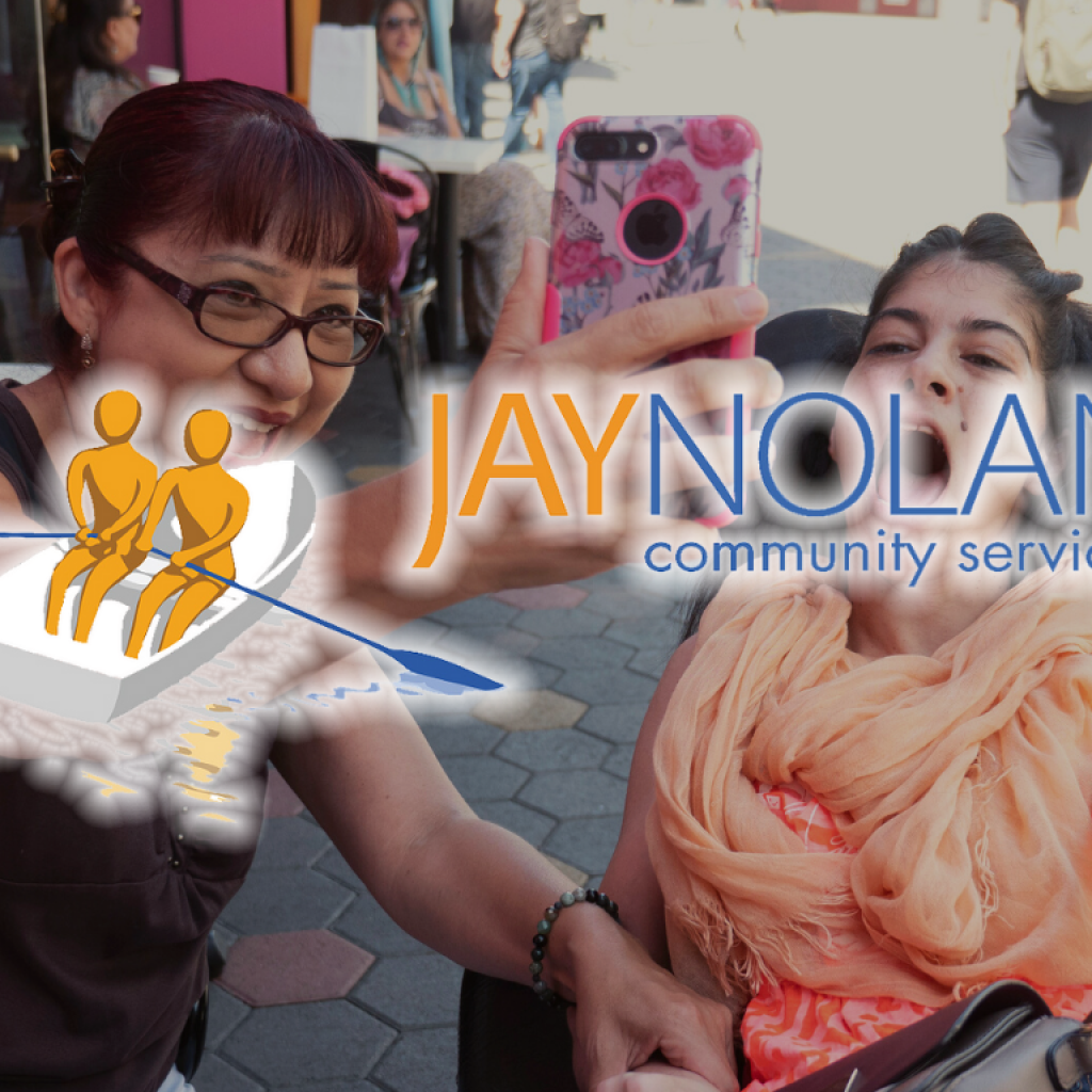 JNCS logo overlaid over an image of a woman holding up a cell phone for a selfie with a woman in an orange scarf in an electronic wheelchair