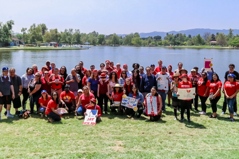 A group photo in front of a lake of around 40 people wearing red and holding signs supporting autism acceptance