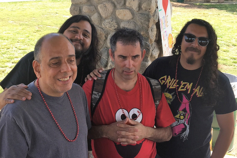 Four men wearing red beaded neclaces standing together at a park