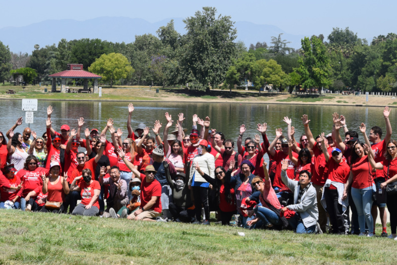 El personal de Jay Nolan y las personas que apoyaron agitaron sus manos mientras posaban para una foto grupal en el picnic de aceptación del autismo de 2022 en el parque.