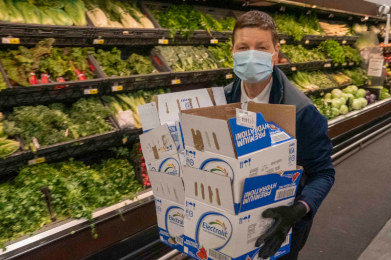 A female employee carrying boxes through the produce aisle at her job in a grocery store