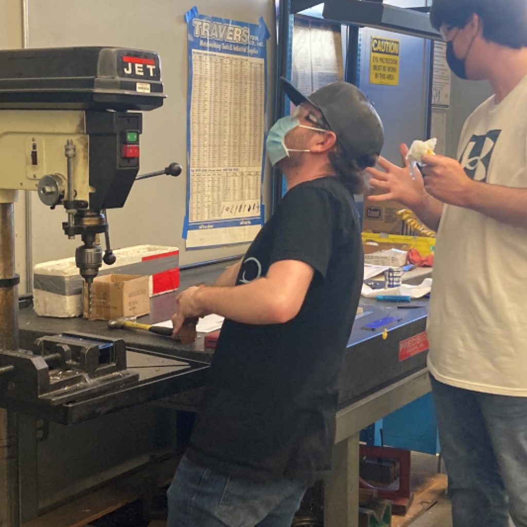 Two young men working with a drill in a machining workshop