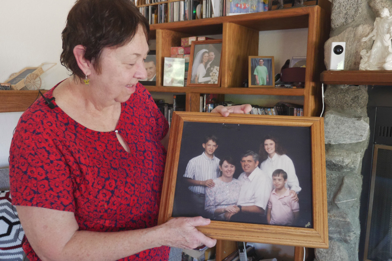 Vicki wearing a floral red blouse proudly holds up a framed photograph of her family.