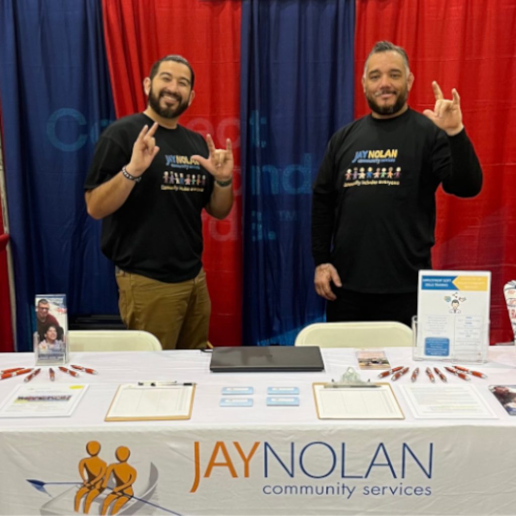 Two JNCS employees holding up the sign language sign for 'love' at the JNCS booth at Deaf Nation 2023