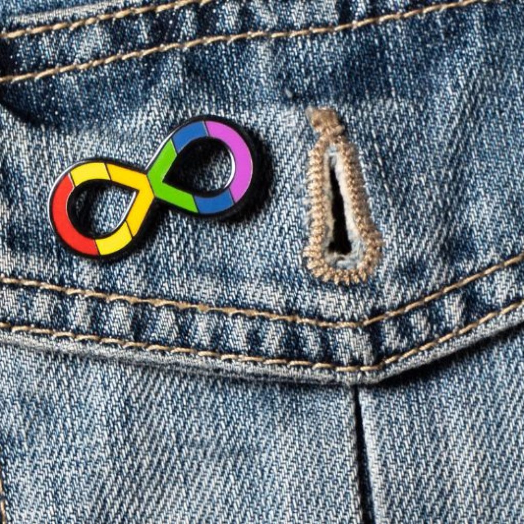 A rainbow infinity pin clipped to denim to commemorate Autistic Pride Day