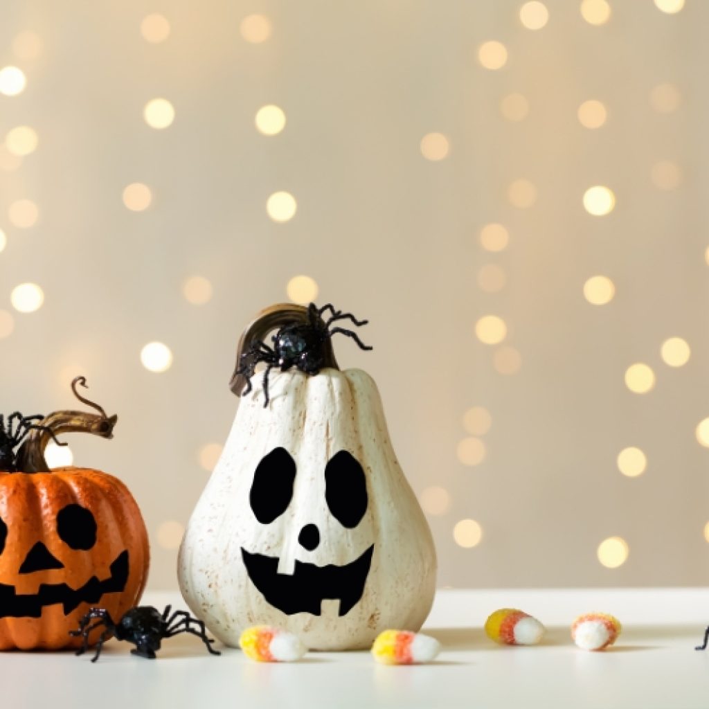 An orange and a white jack-o-lantern surrounded by candy corn.