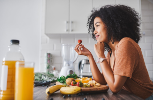 Mujer comiendo una fresa en la mesa de su cocina con un desayuno saludable frente a ella.