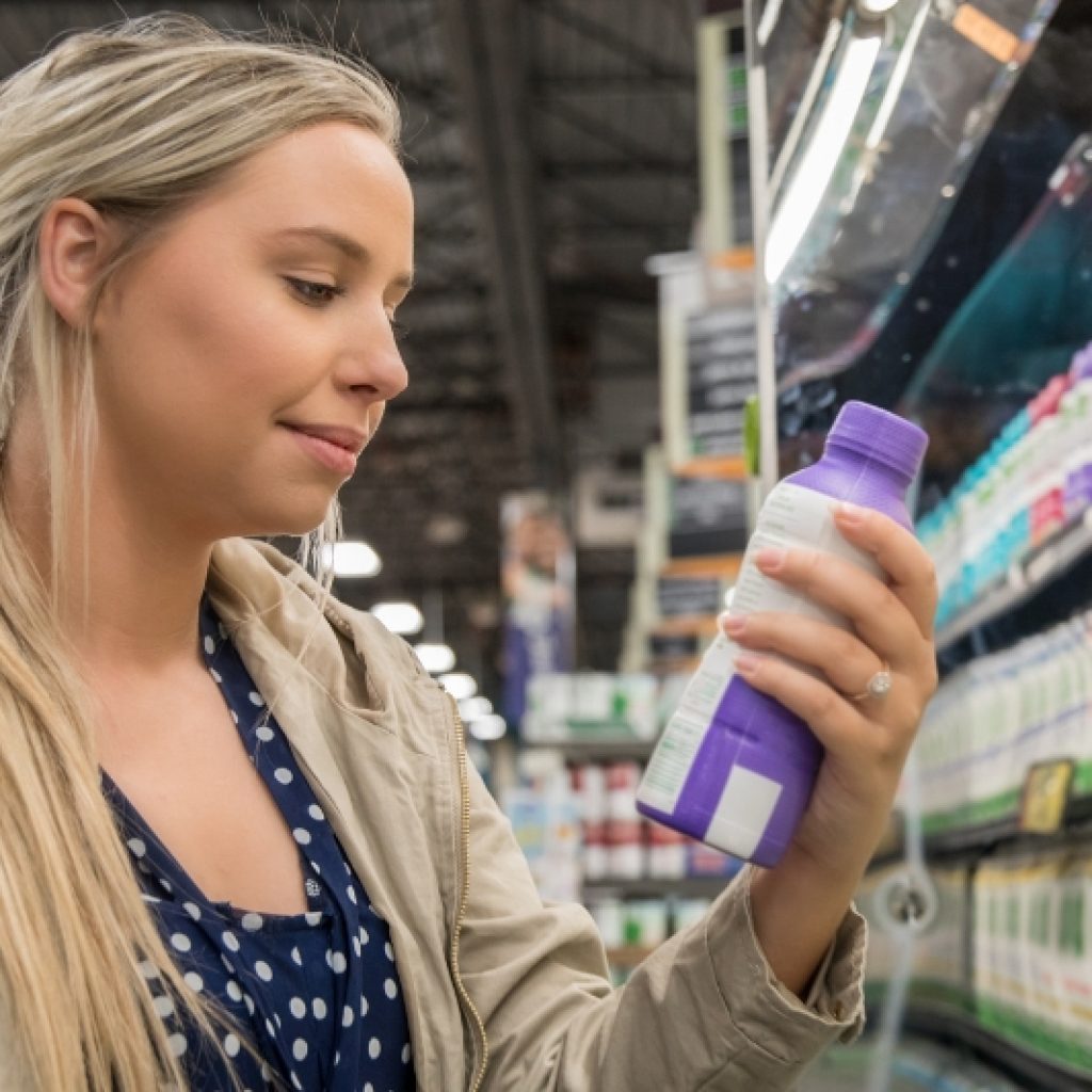 Caucasian woman reading the nutrition label on a purple bottle of juice at a grocery store.