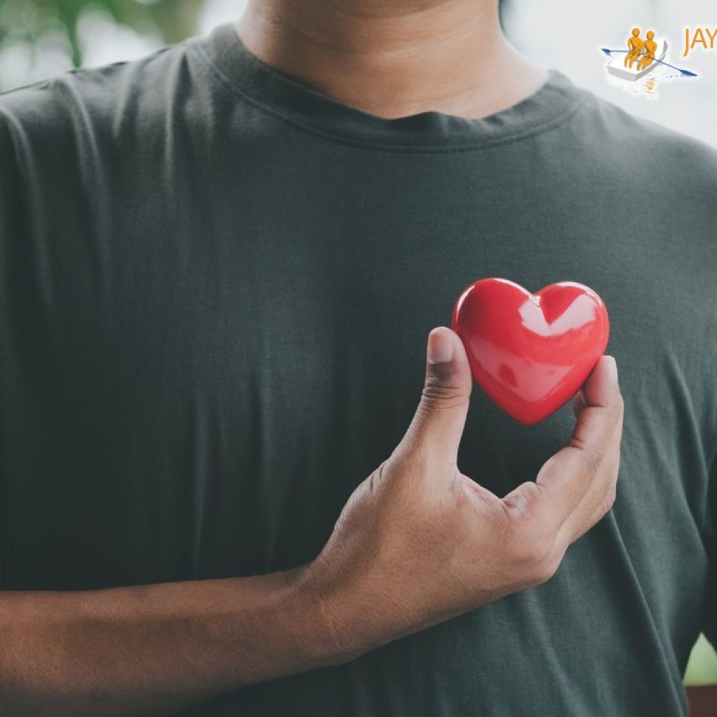 An African American man wearing a black t-shirt holding a red heart over his heart.