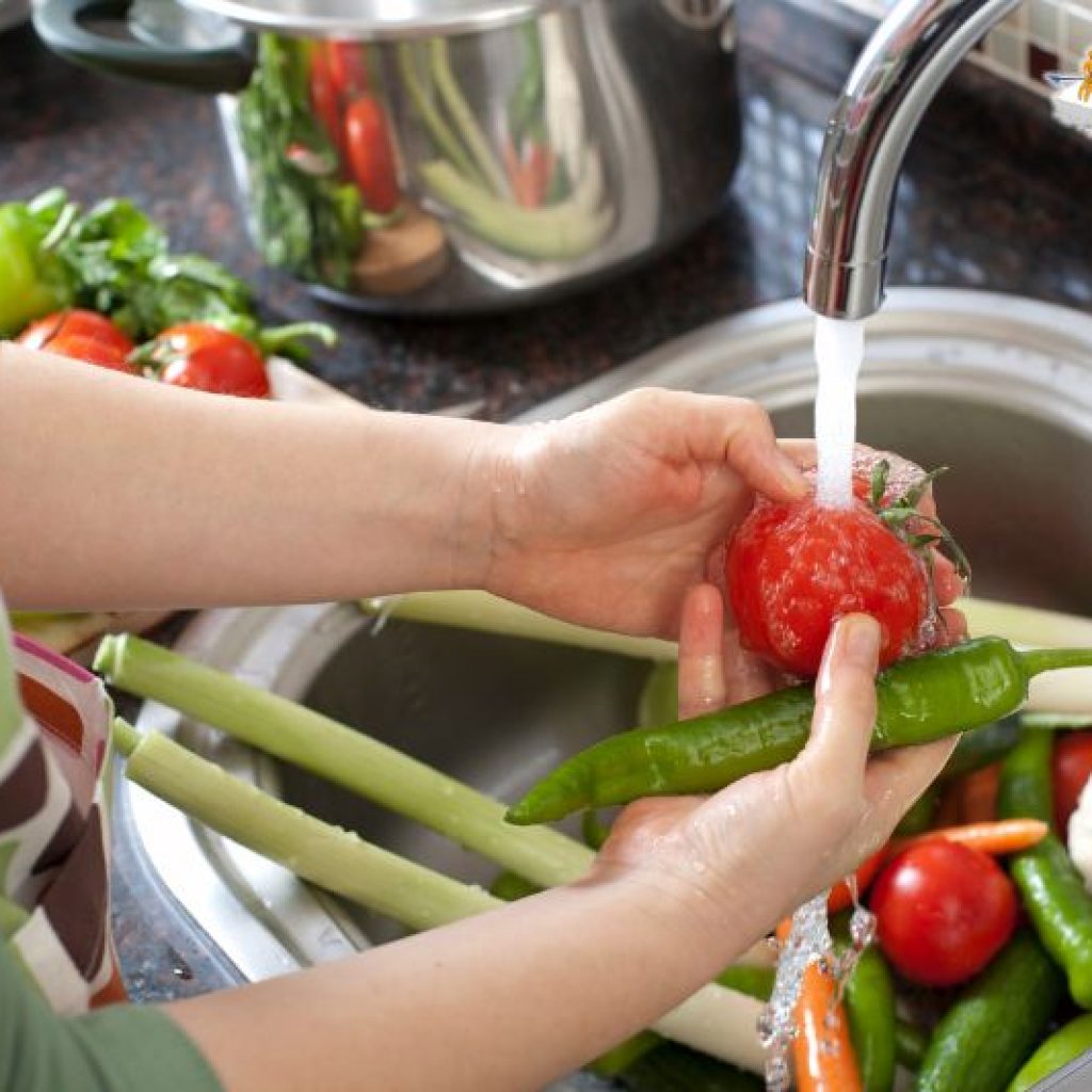 a pair of hands washing various vegetables in a metal sink.