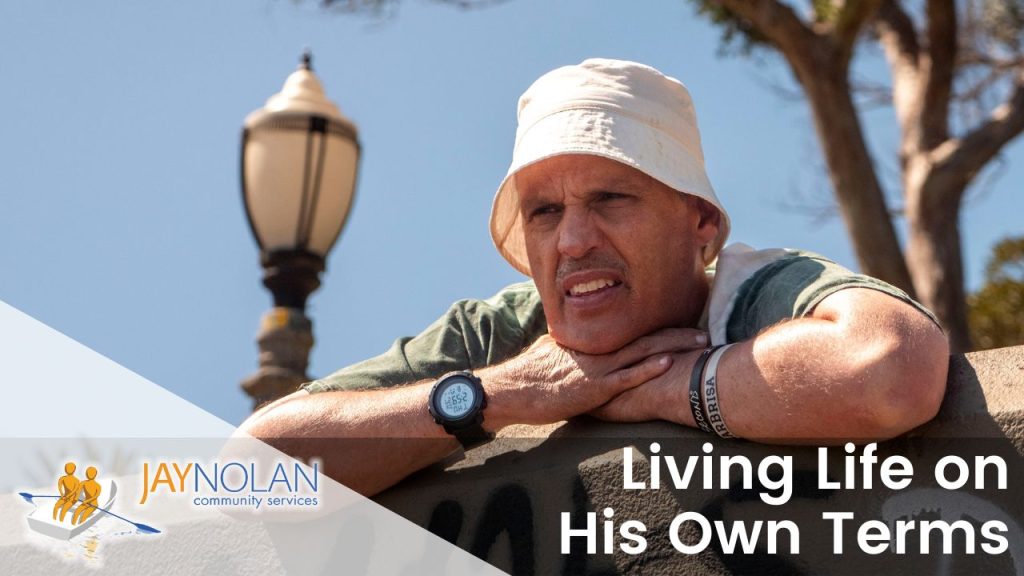 Video Thumbnail featuring Bobby, an older Caucasian man wearing a white hat and a striped green and white shirt leaning against a wall at a park. Text reads: "Living Lie on His Own Terms"