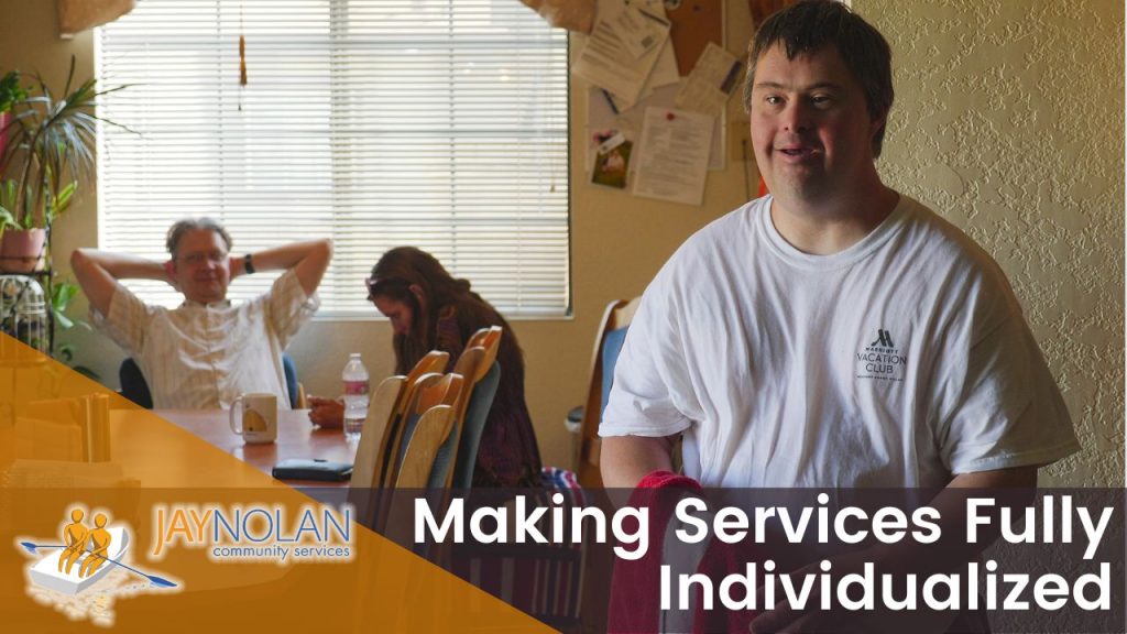 Video thumbnail featuring a Caucasian man in white t-shirt standing in his kitchen with his family sitting around a dining table in the background. Text reads: "Making Services Fully Individualized"