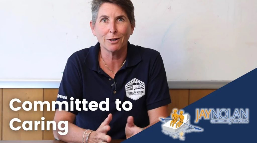 Video Thumbnail of a Caucasian woman with short grey hair wearing a dark blue polo shirt. Text reads: "Committed to Caring"