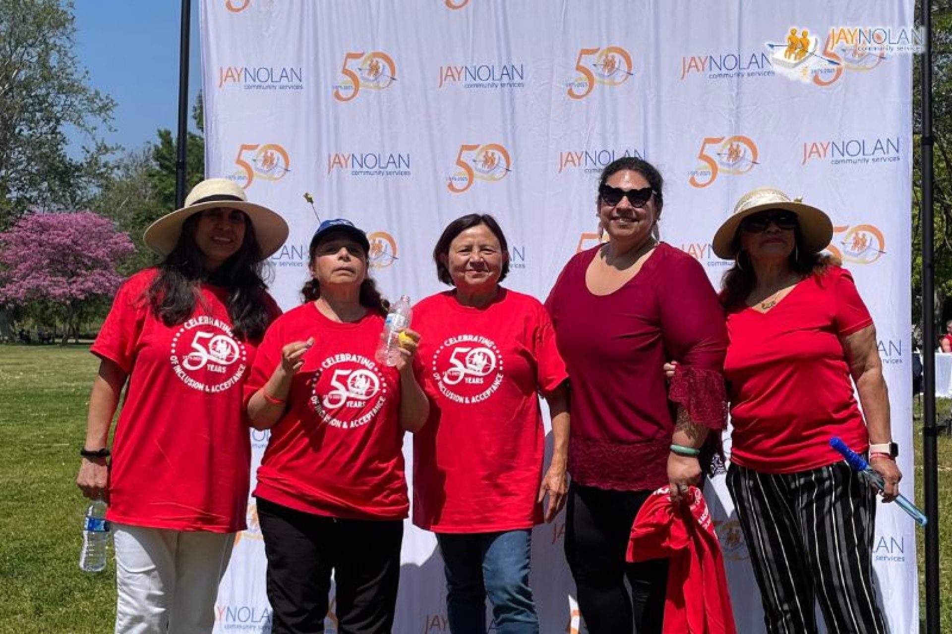 Five adults all wearing red posing in front of a Jay Nolan step and repeat backdrop