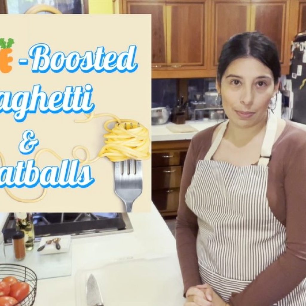 Thumbnail for a recipe video with woman with dark hair wearing and striped apron standing in a kitchen. Text reads: "Veggie-Boosted Spaghetti and Meatballs"