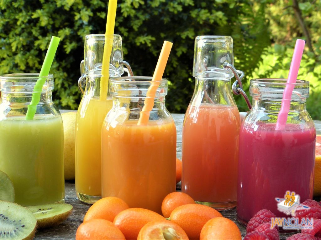 beverages-blog-featured-image Five glass bottles of different colored juice sitting on a table surrounded by fruit.