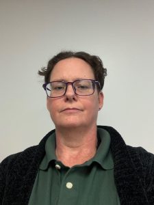Portrait of New Jay Nolan Clinical Director Jei Manley-Stanley, middle aged Caucasian female with short brown hair wearing a green polo shirt and glasses.