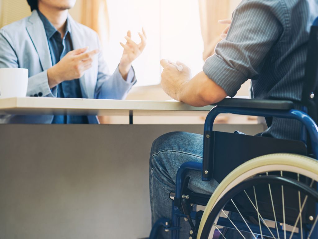 Professionally dressed man in a wheelchair talking to another professional at their desk