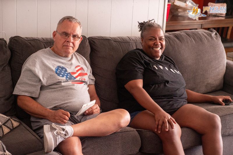 African American woman and Caucasian man sitting on a dark brown couch together.