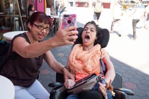 Example of a Direct Support Professional job, female DSP taking a selfie with the young woman that she supports. The young woman is in a wheelchair.