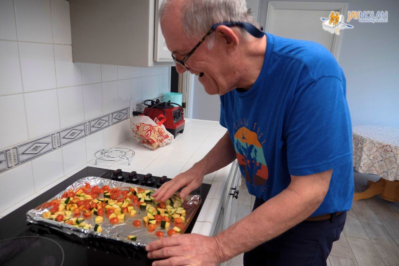 Older white man in a blue t-shirt preparing vegetables for roasting