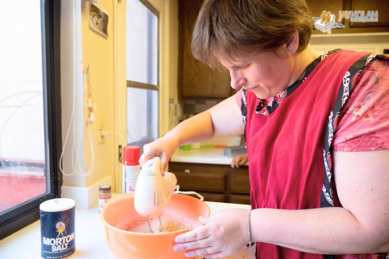 Caucasian woman wearing a red apron using a mixer to mix up batter in a mixing bowl