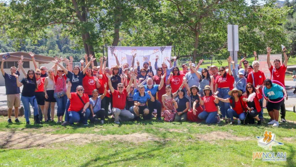 A group of Jay Nolan staff posing with their arms in the air for a group photo at the Autism Acceptance Picnic